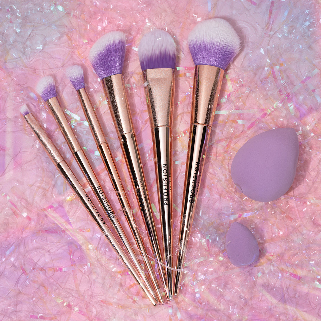 Makeup brushes with purple bristles and rose gold handles, alongside purple makeup sponges.