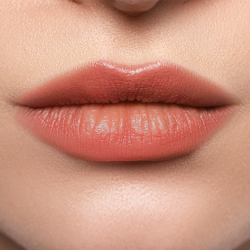 Close-up of lips wearing Profusion Peach Glaze, showing a soft peachy shine and smooth finish.