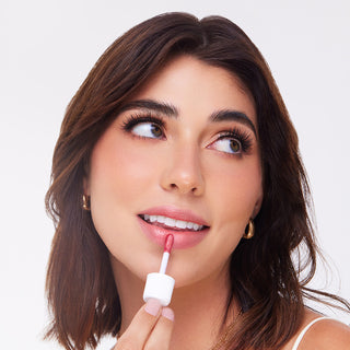Woman applying Profusion Cosmetics Lip Glaze in a shimmering pink shade.