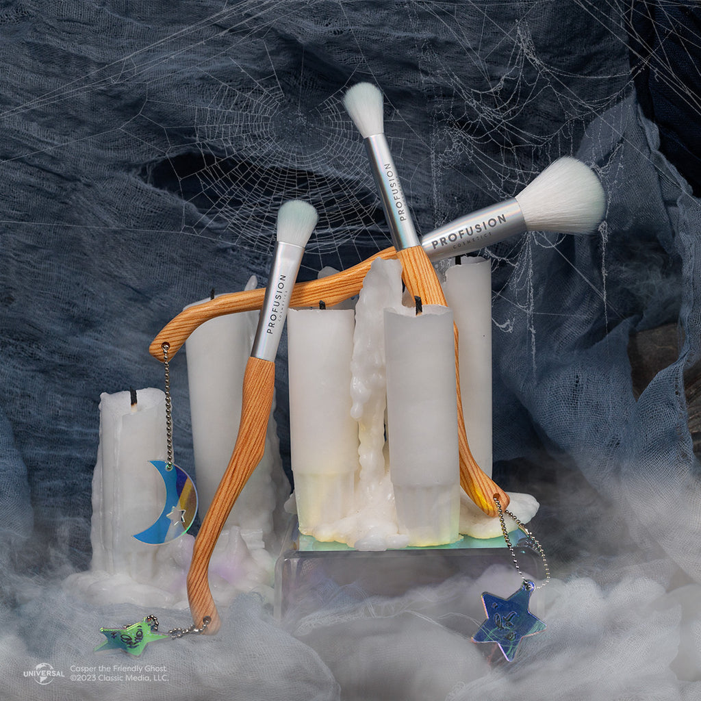 three makeup brushes posed in with white candles, smoke on the bottom of the picture, and spiderwebs as a backdrop