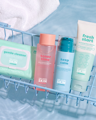 Five skincare products from The Skin Platform are arranged in a light blue wire bath basket over water. The products include a green gentle cleanse pack, a pink toner bottle, a light blue keep calm bottle, and a white fresh start exfoliating wash tube.