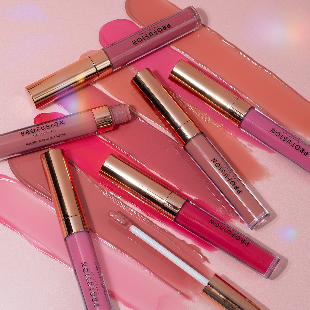 Lip glosses in various pink shades with gold caps, arranged on swatches of matching colors.